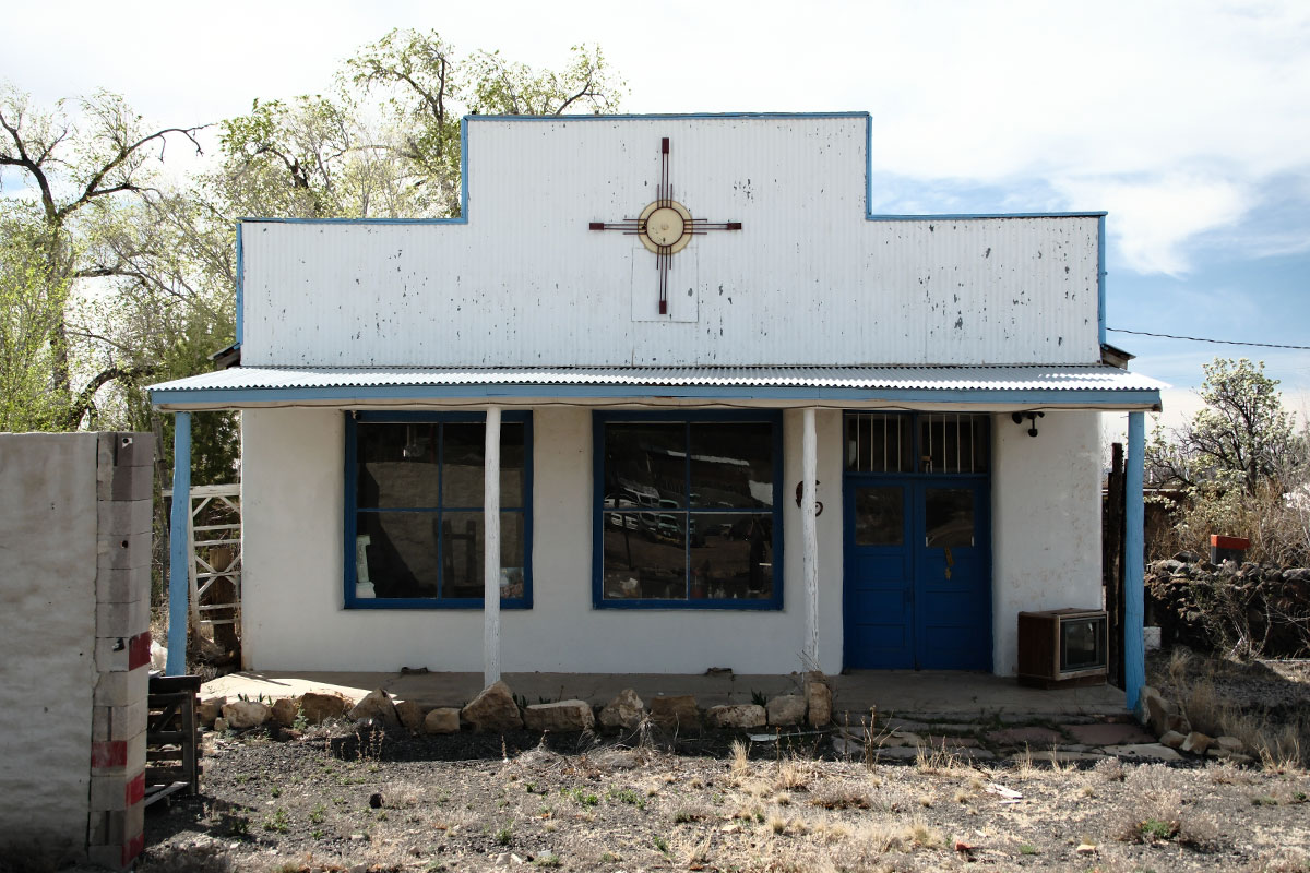 Una tienda de adobe blanca con fachada falsa, puertas y marcos de ventanas azules y un símbolo de sol en la fachada