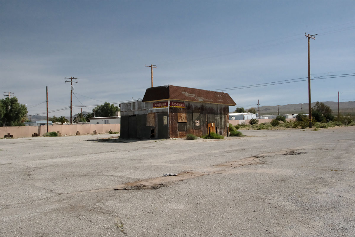 Un edificio Food Mart tapiado, solo en una explanada agrietada y vacía, con colinas del desierto detrás