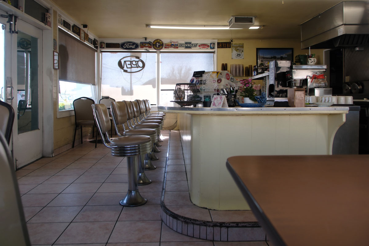 La barra vacía y los bancos cromados de un diner pequeño, con el letrero de Open en la ventana