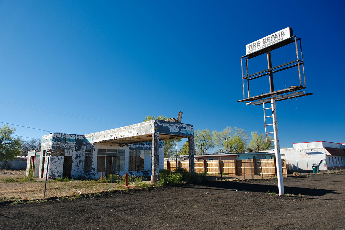 La gasolinera Whiting Bros abandonada en Holbrook, un edificio de techo plano con la pintura descascarada y una marquesina, junto a un poste alto con un letrero Tire Repair