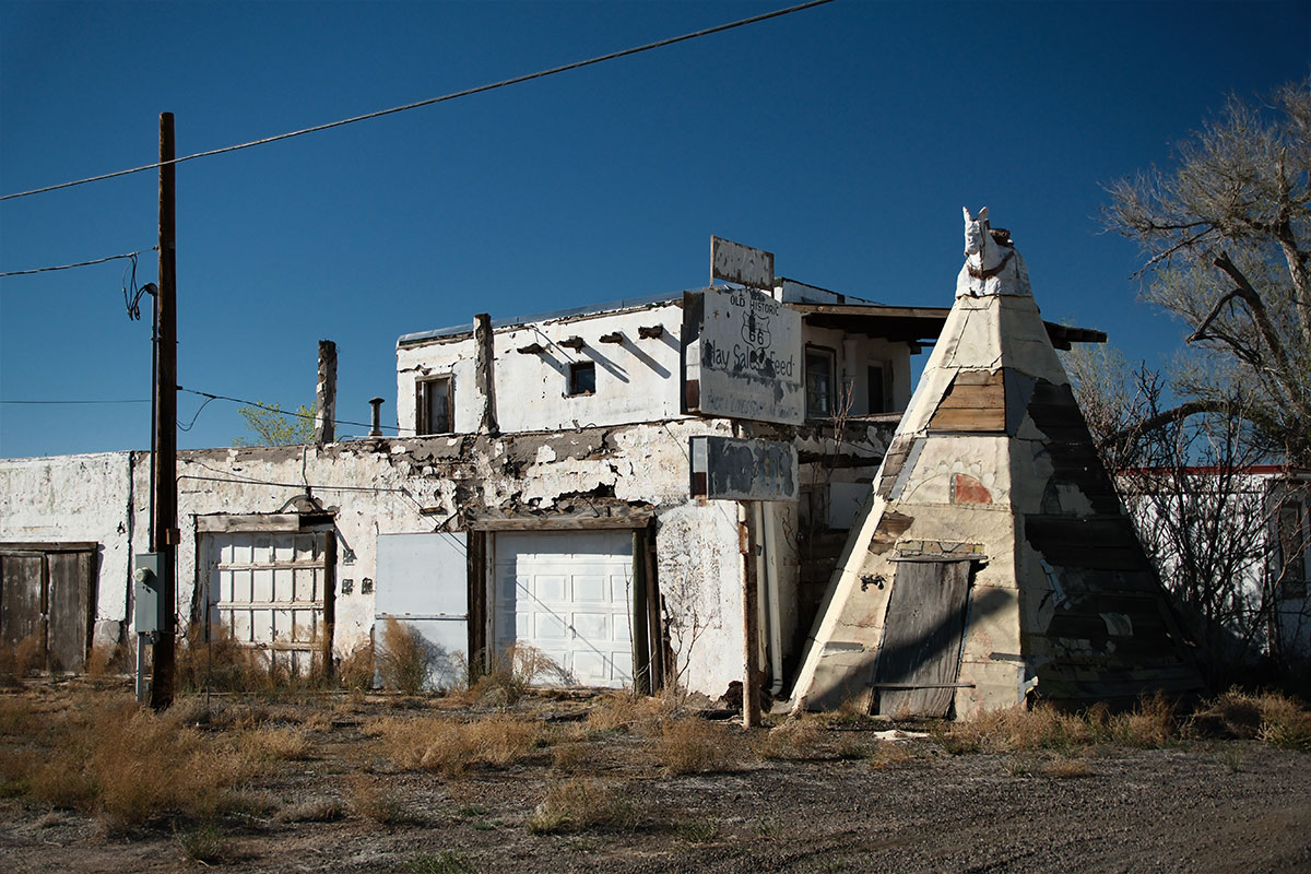 Un edificio blanco descascarado con un letrero de Hay Sale and Feed y un tipi de madera desgastada coronado por la figura de un caballo blanco