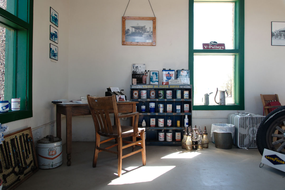 Dentro de la estación restaurada: un escritorio y una silla de madera, repisas con latas de aceite antiguas y ventanas con marcos verdes