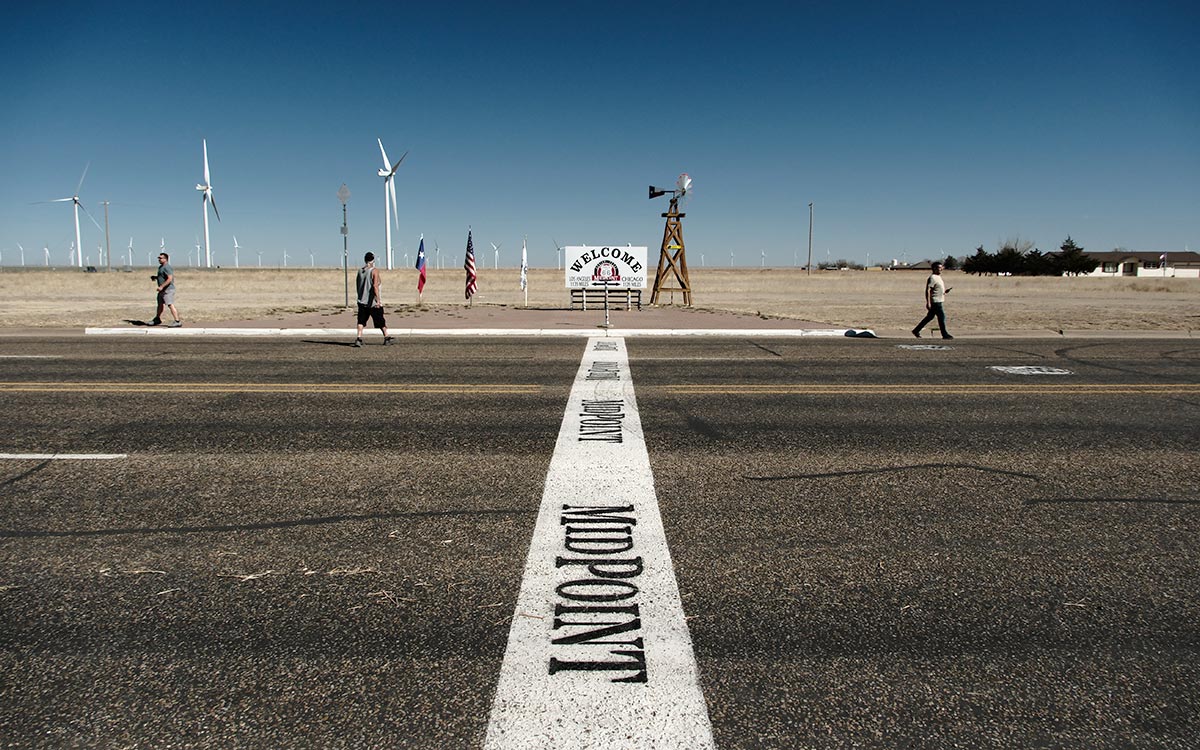 La palabra Midpoint pintada sobre la Route 66 en Adrian, Texas, con el letrero de Midpoint al fondo