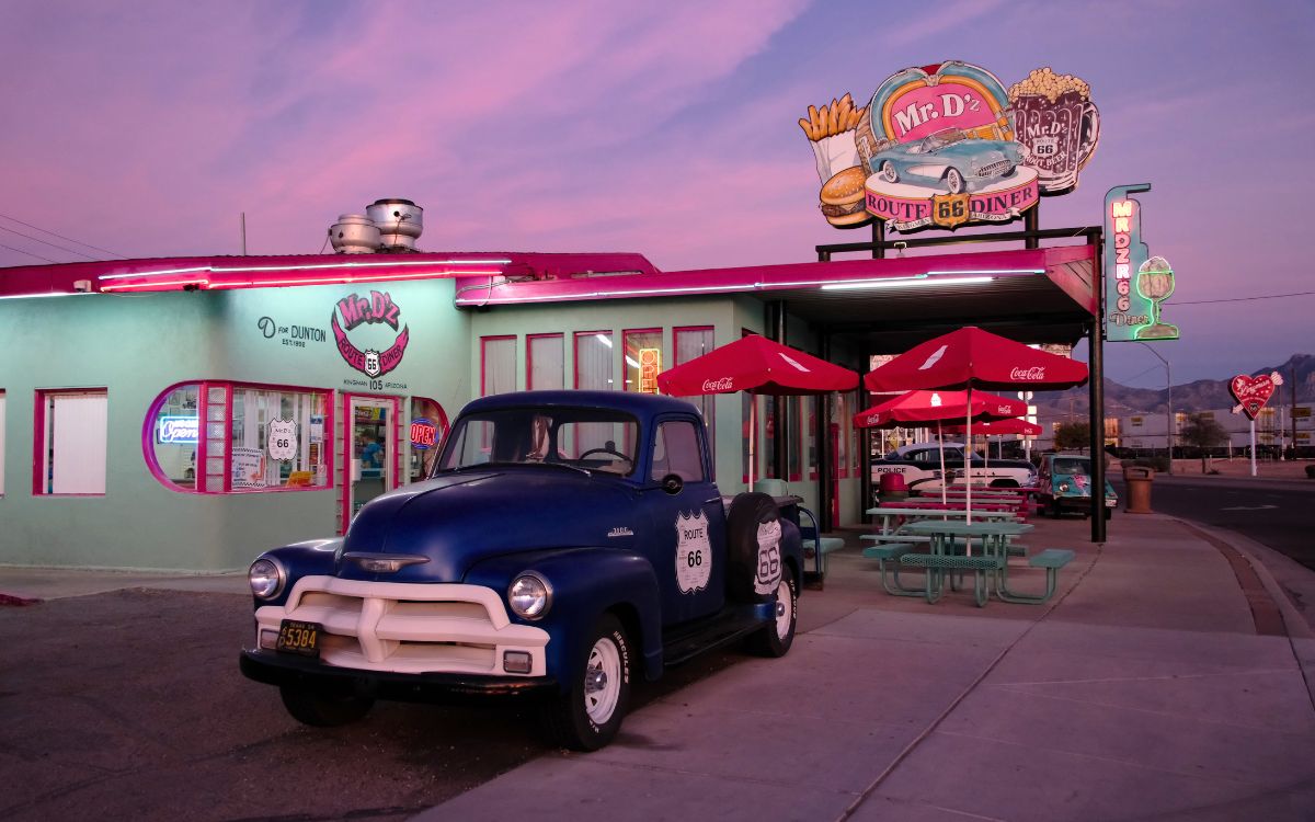 Mr. D’z Route 66 Diner en Kingman, Arizona, rosa y turquesa al atardecer, con una camioneta antigua al frente