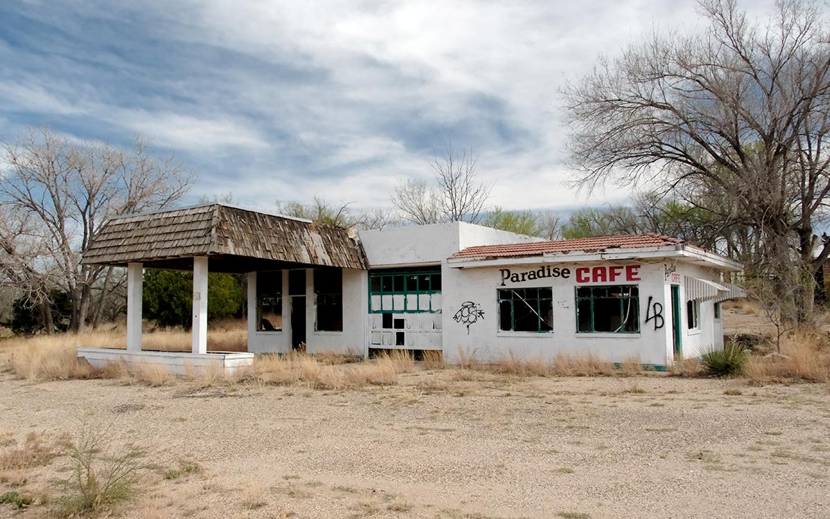 El Paradise Cafe abandonado, con las ventanas rotas y las paredes marcadas con grafitis, entre hierba seca bajo un cielo nublado