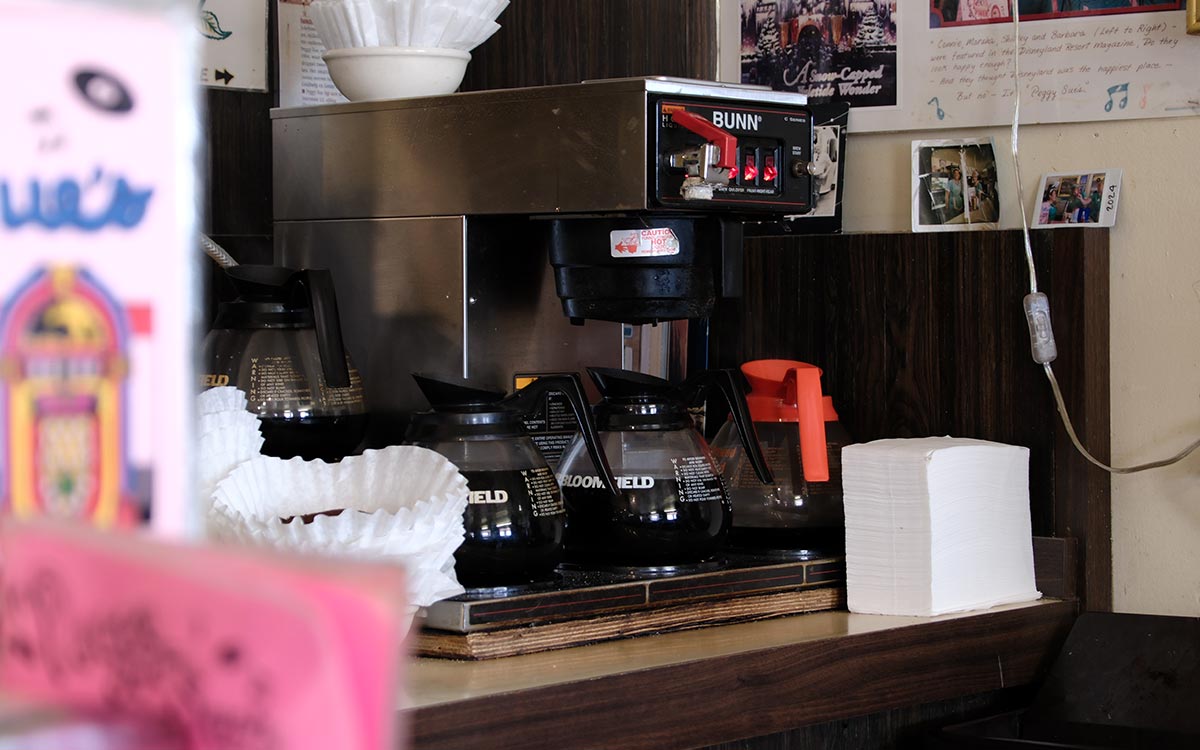 La estación de café detrás del mostrador del diner Peggy Sue’s, con jarras de vidrio sobre la placa caliente y pilas de filtros