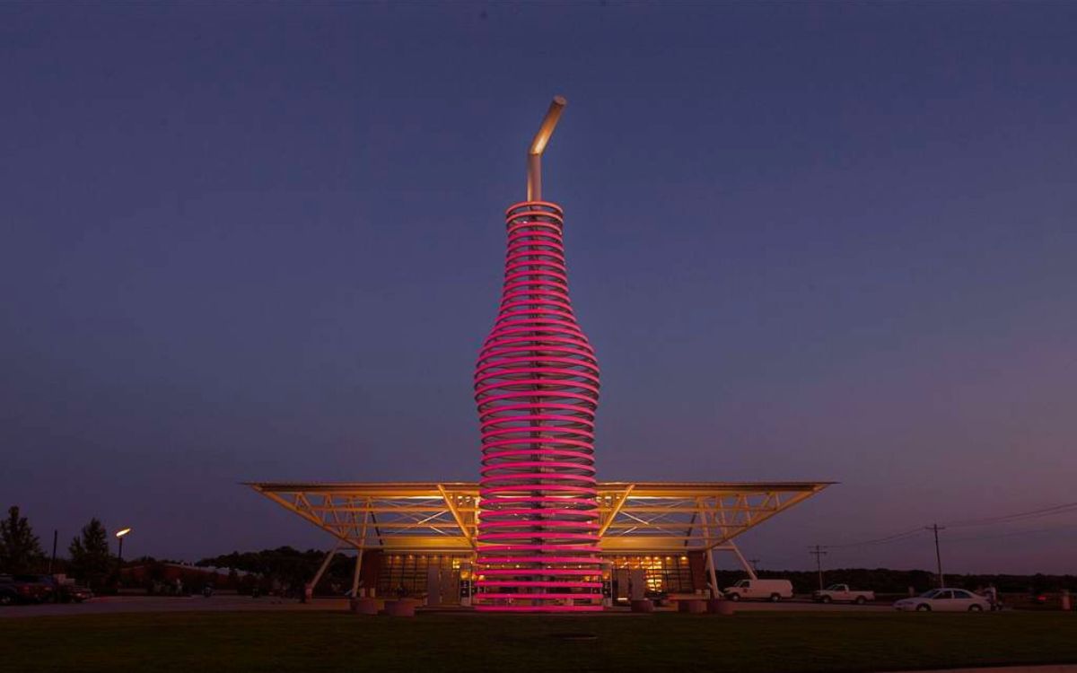 La botella gigante de refresco de POPS en Arcadia, Oklahoma, brillando en rosa bajo su marquesina de acero al atardecer