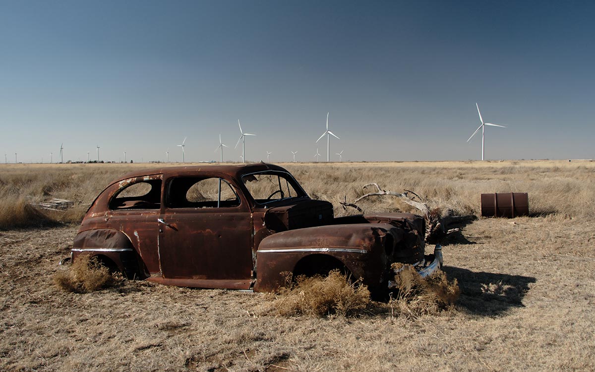 Un auto oxidado de los años cuarenta en el pasto seco, bajo aerogeneradores y un cielo azul intenso