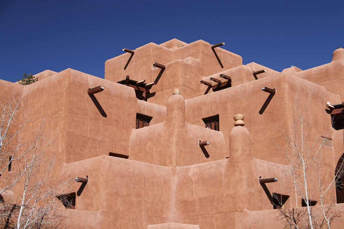 Un edificio de varios pisos de estilo Pueblo Revival en Santa Fe, con muros de adobe escalonados y vigas de madera que sobresalen contra un cielo azul intenso