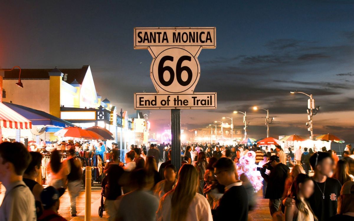 El letrero Santa Monica 66 End of the Trail en el muelle al atardecer, con gente abajo