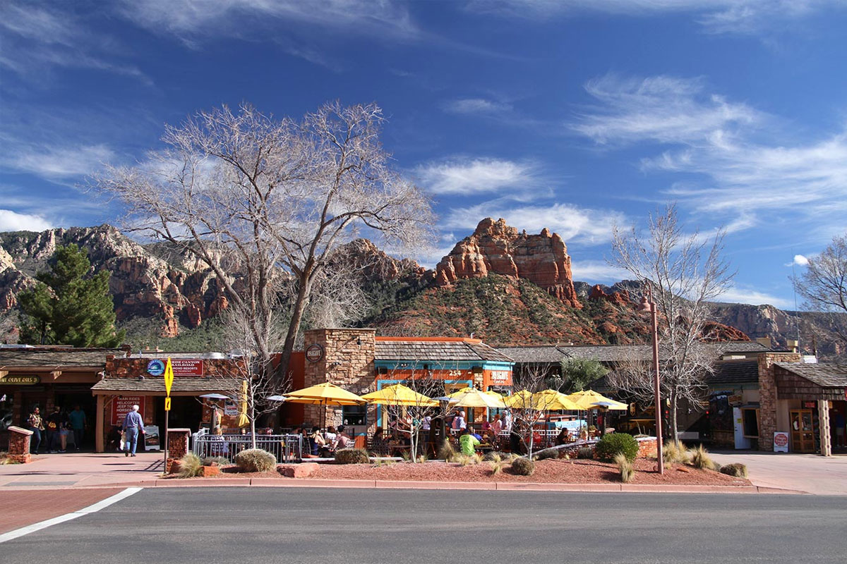 Terrazas de café con sombrillas amarillas en una calle de Sedona, con cerros de arenisca roja al fondo