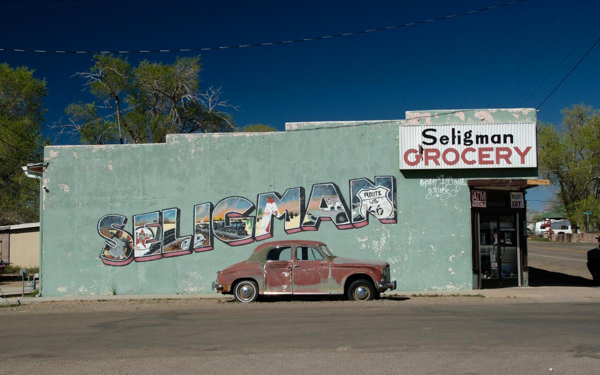 El edificio de Seligman Grocery con un mural pintado de Seligman y un viejo auto oxidado estacionado al frente
