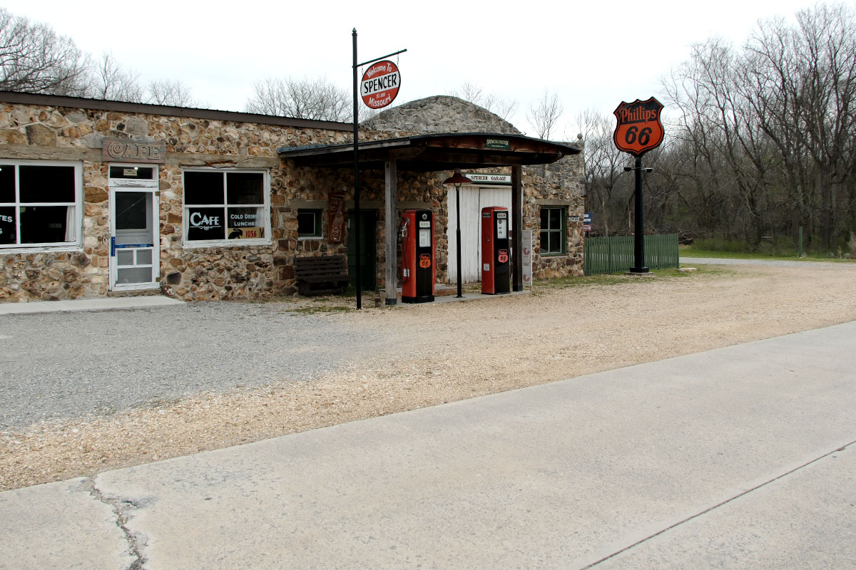 Un café y taller de piedra con bombas de gasolina rojas de época y un letrero de Phillips 66 junto al viejo camino