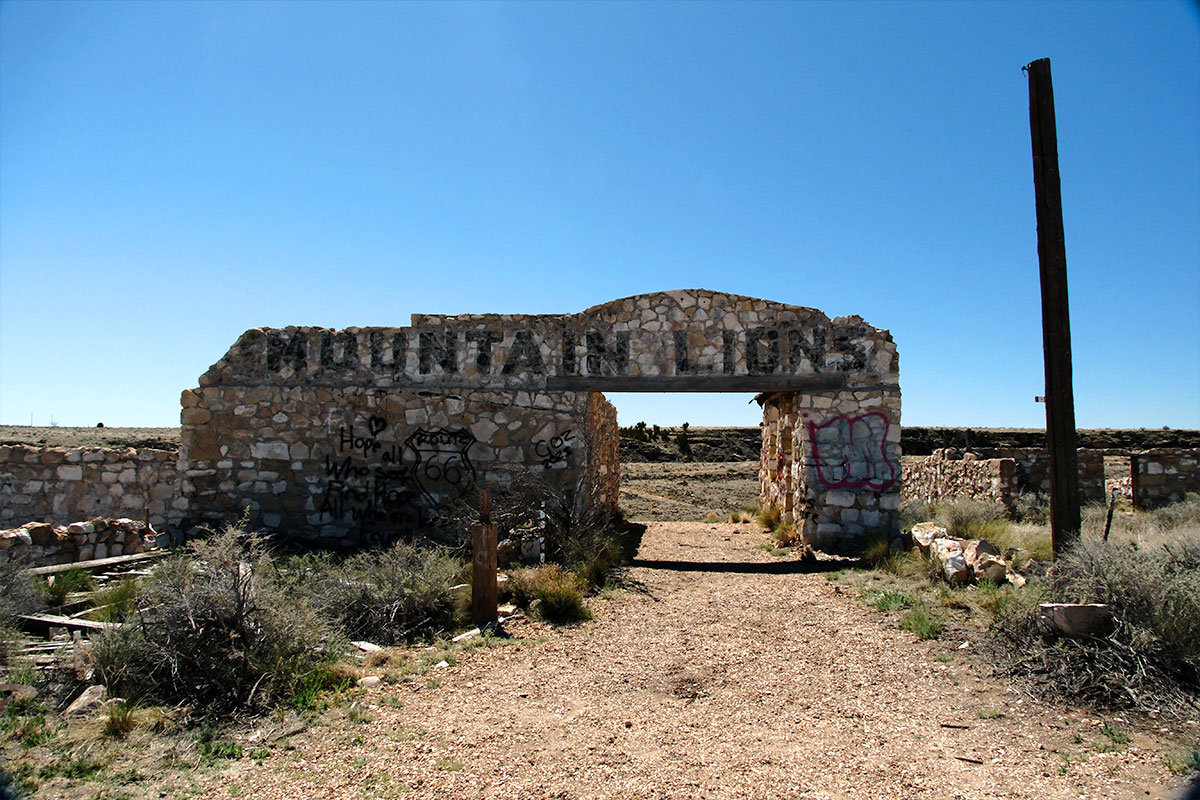 Un arco de piedra desmoronado, pintado con las palabras MOUNTAIN LIONS y cubierto de grafitis, en la entrada de los antiguos recintos de animales de Two Guns