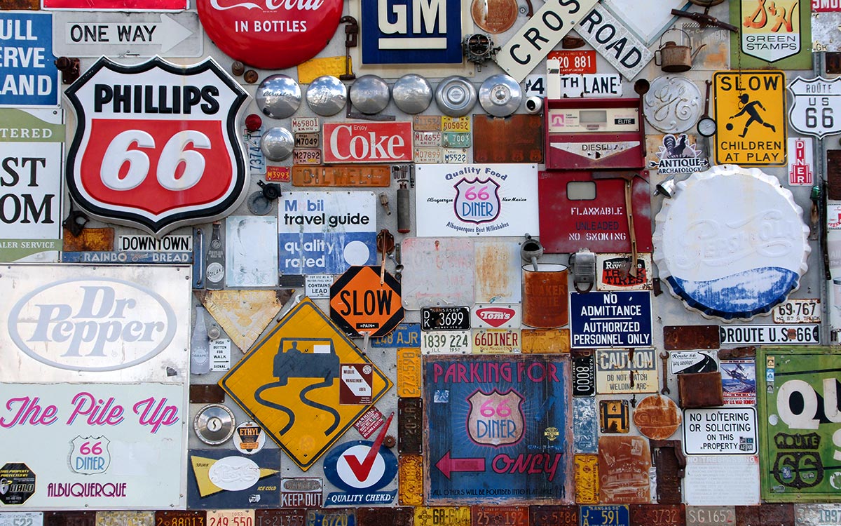 Una pared cubierta de letreros antiguos: Phillips 66, Coke, señales de carretera y placas de matrícula viejas