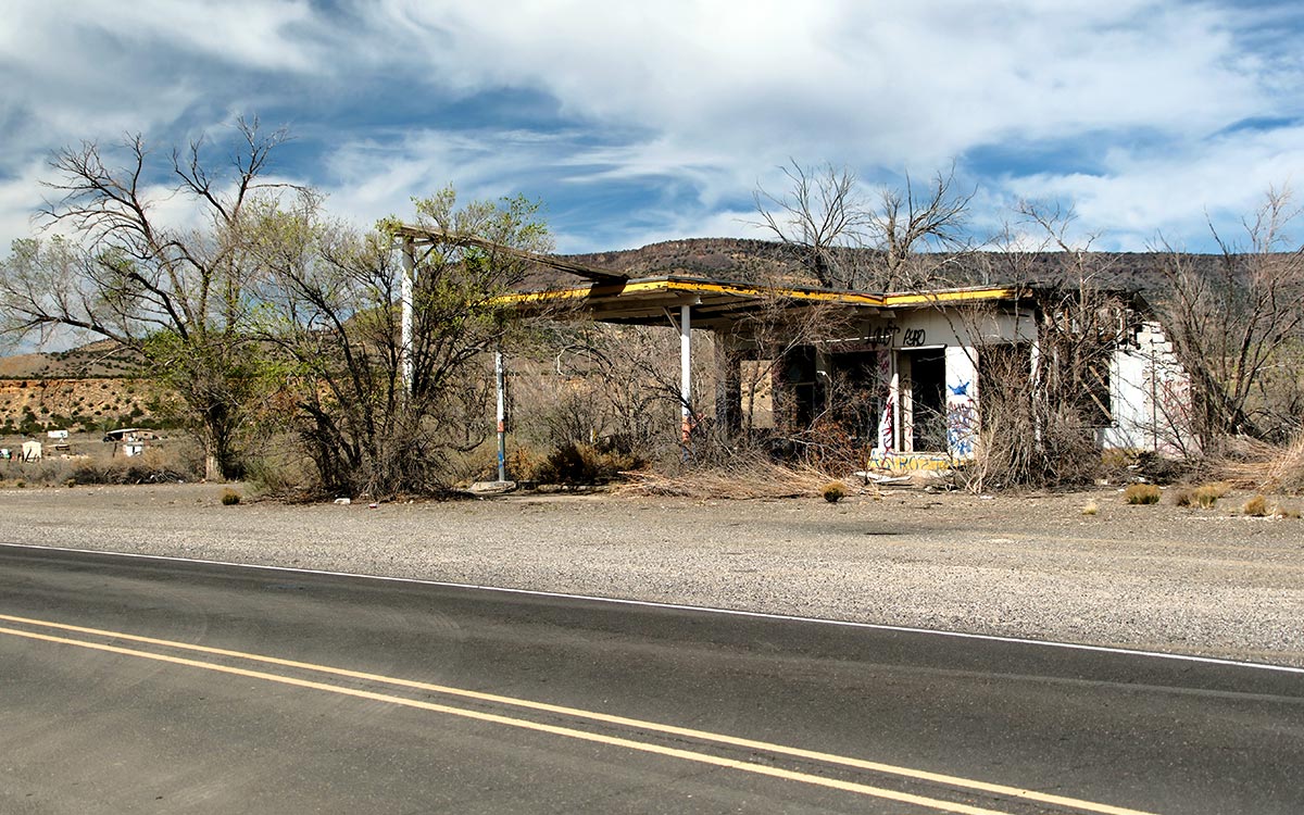 La carcasa abandonada de una gasolinera Whiting Bros., con su marquesina amarilla invadida por árboles