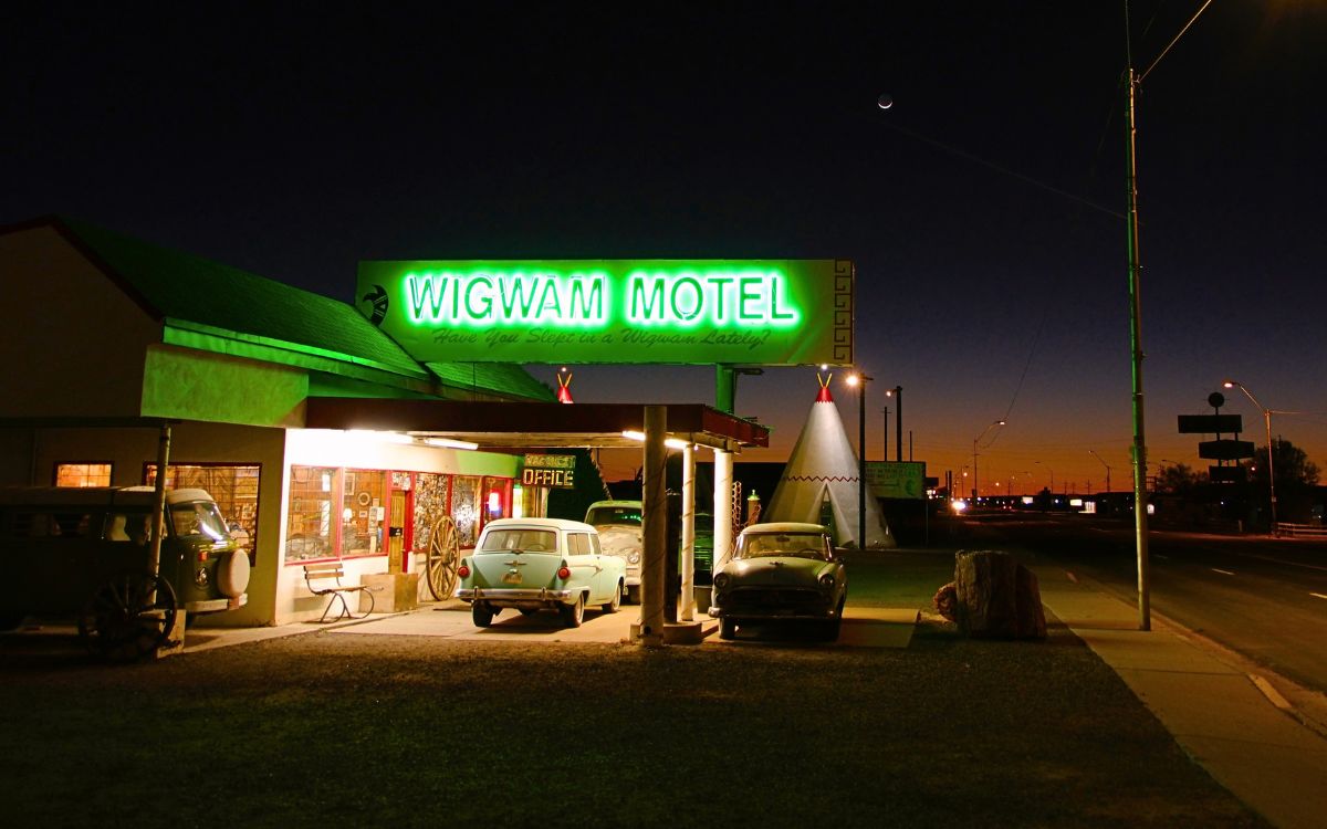 El letrero de neón verde del Wigwam Motel encendido de noche, con autos antiguos estacionados frente a la oficina
