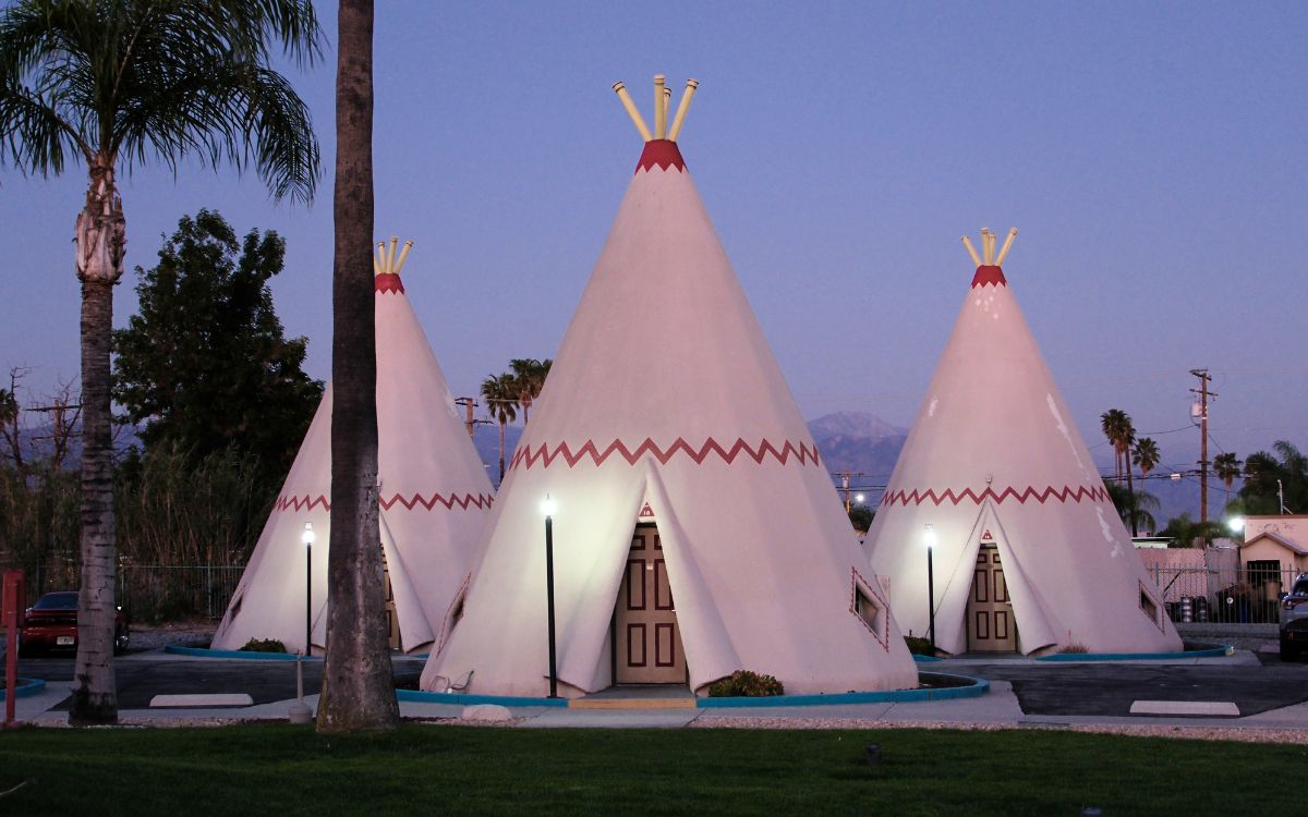 Tres wigwams de concreto iluminados al atardecer entre palmeras en el Wigwam Motel de Rialto, California