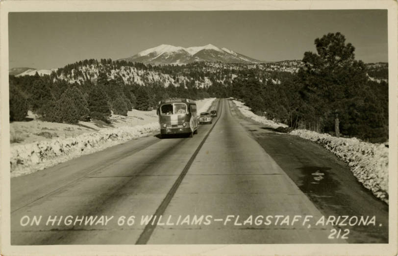 Una postal fotográfica antigua de un autobús en la nevada Highway 66 entre Williams y Flagstaff, Arizona, con los San Francisco Peaks al fondo